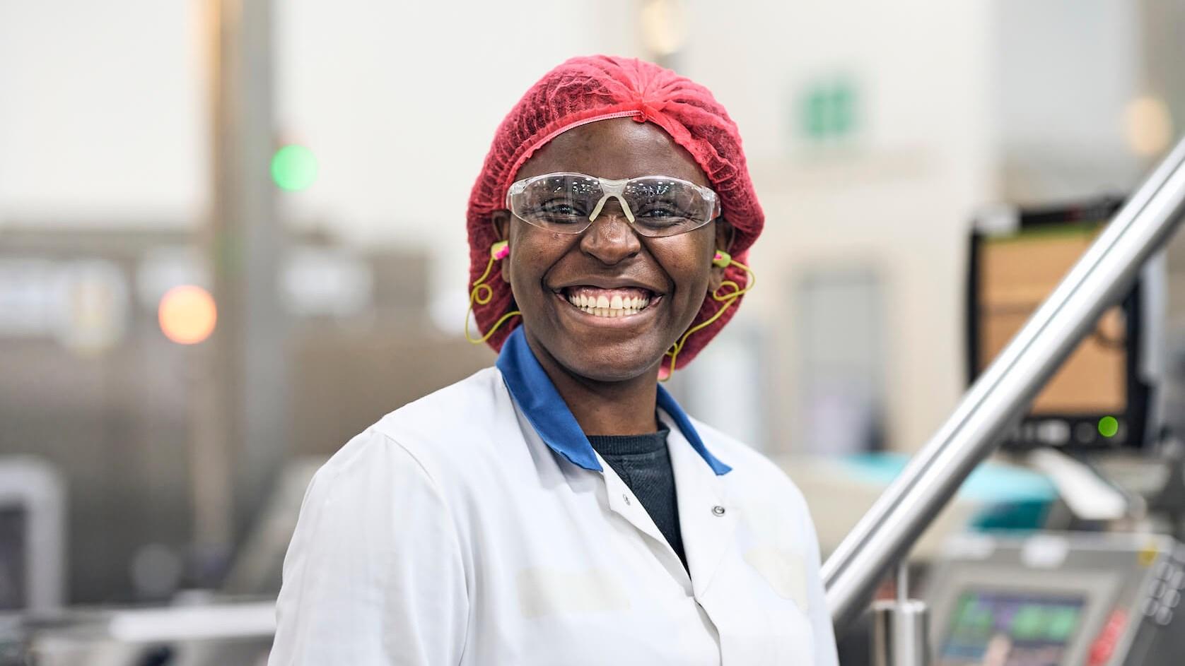 Female Reckitt employee in a hairnet, lab coat and earplugs smiling in a laboratory setting