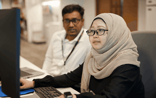 Woman in headscarf uses the computer next to Asian male colleague